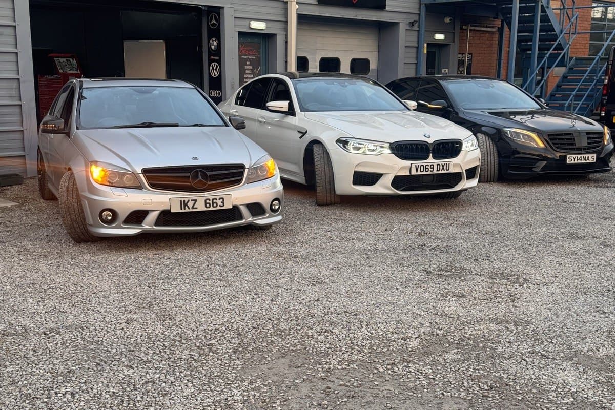 A Mercedes-AMG, a BMW M5 and a Mercedes S-Class parked outside the Team Mercedes Cardiff workshop with their lights on