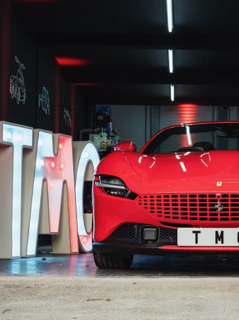 A Ferrari inside the Team Mercedes Cardiff workshop, beside the illuminated TMC letters