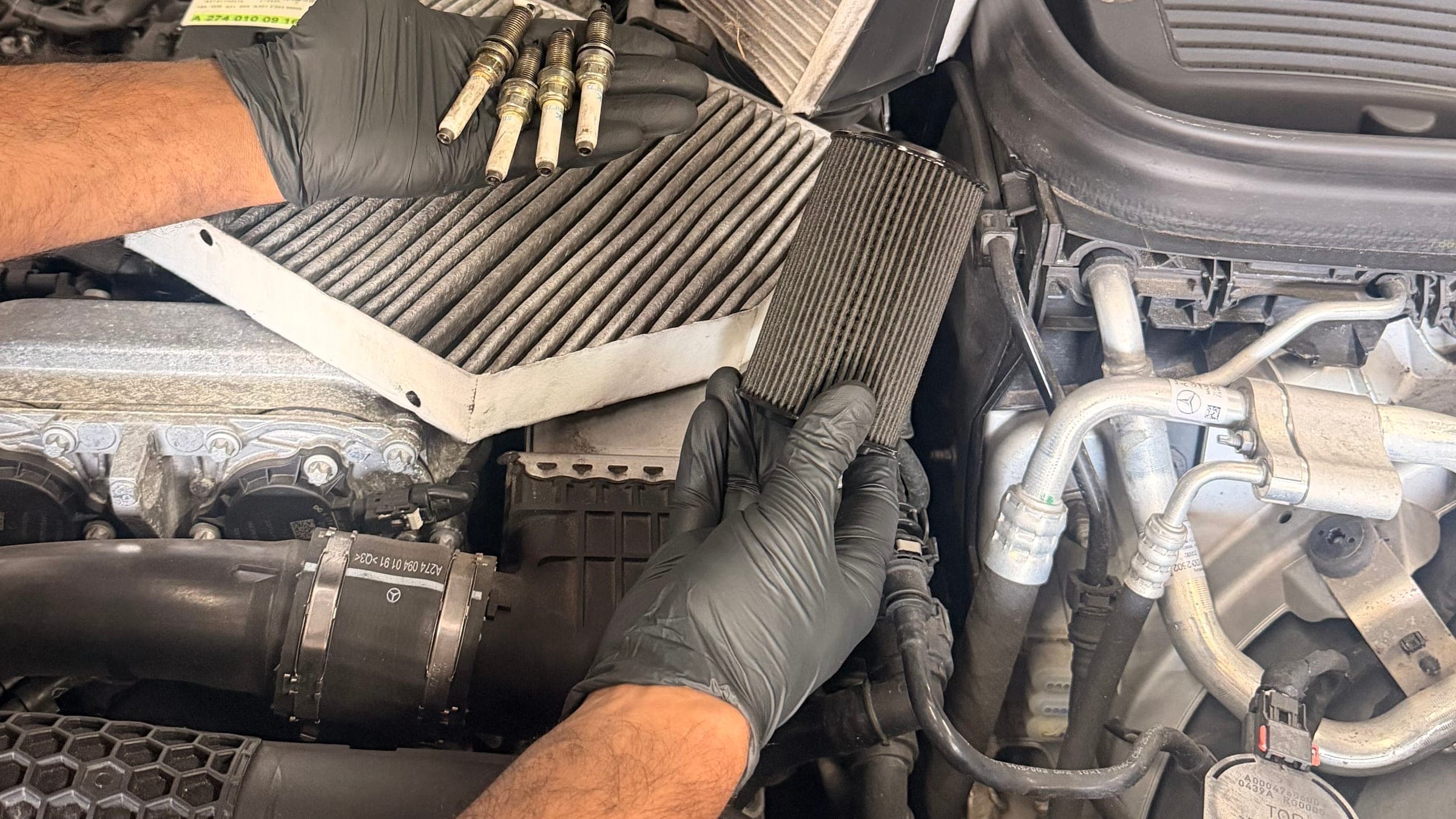A used and a replacement filter held side by side over an open Mercedes engine bay