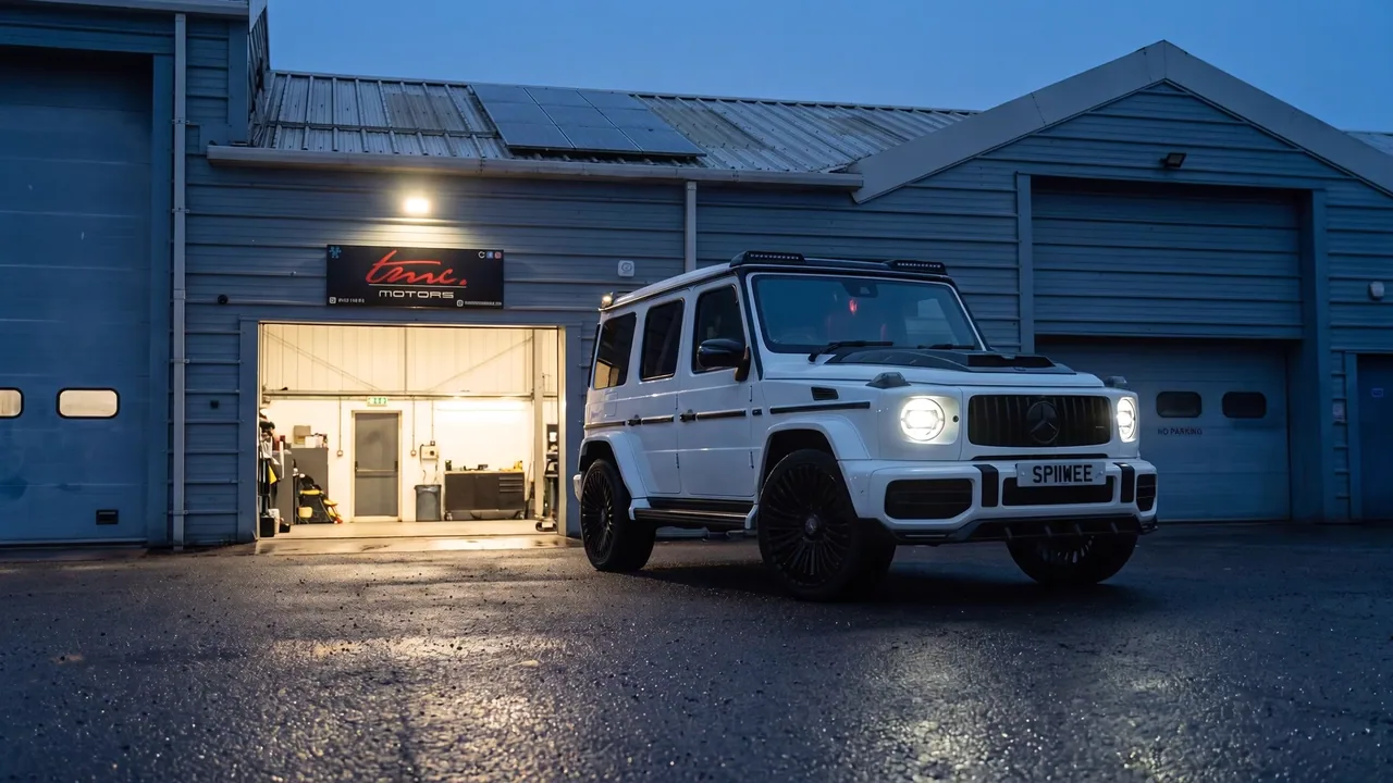 A Mercedes G-Class pulling away from the lit Team Mercedes Cardiff workshop at dusk